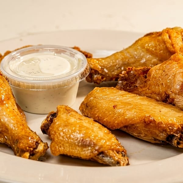 Golden-brown chicken wings and drumettes on a white plate with a side of ranch dressing.