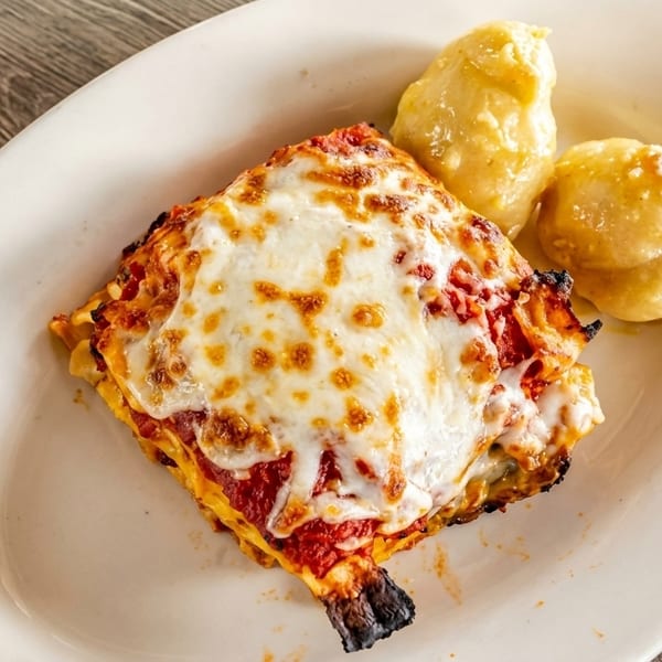 A serving of lasagna with melted cheese and two garlic knots on a white oval plate.