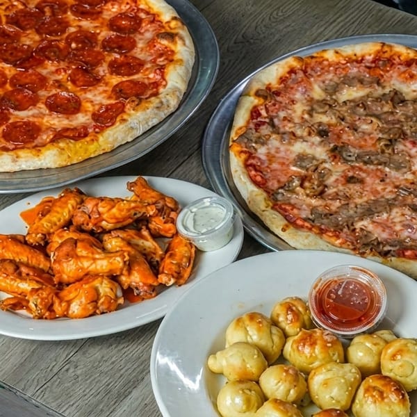 Two pizzas, one pepperoni and one steak, with a plate of buffalo wings and garlic knots.
