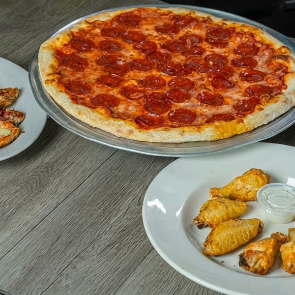 A pepperoni pizza, chicken wings with ranch, and cheesy bread on a wooden table.