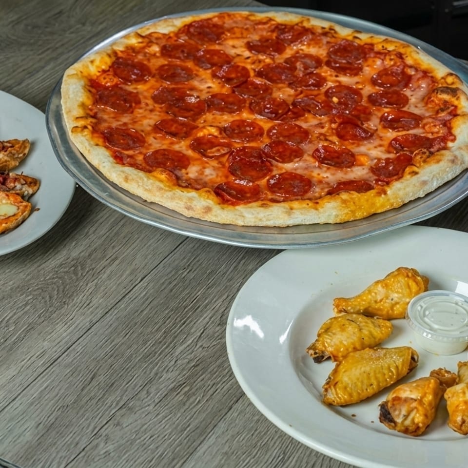 A pepperoni pizza, chicken wings with ranch, and cheesy bread on a wooden table.
