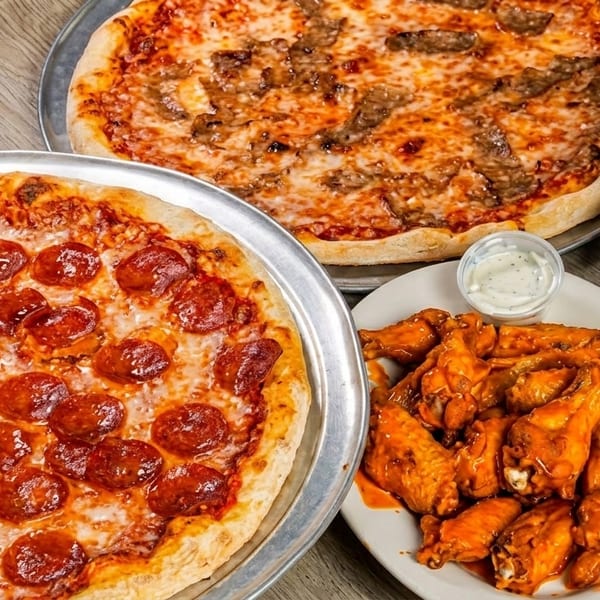 Two pizzas, one pepperoni and one sausage, with buffalo wings and garlic knots on a wooden table.
