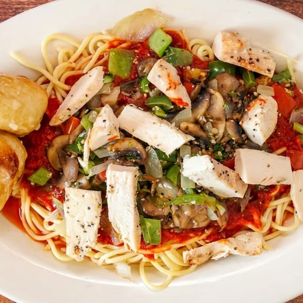 Spaghetti with chicken, mushrooms, peppers, onions, and tomato sauce, served with two bread rolls.