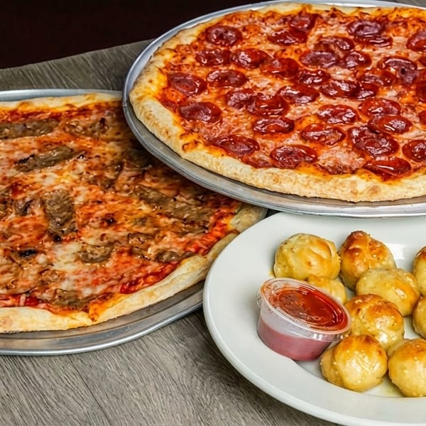 Two pizzas, one pepperoni and one with steak, alongside a plate of garlic knots with marinara sauce.