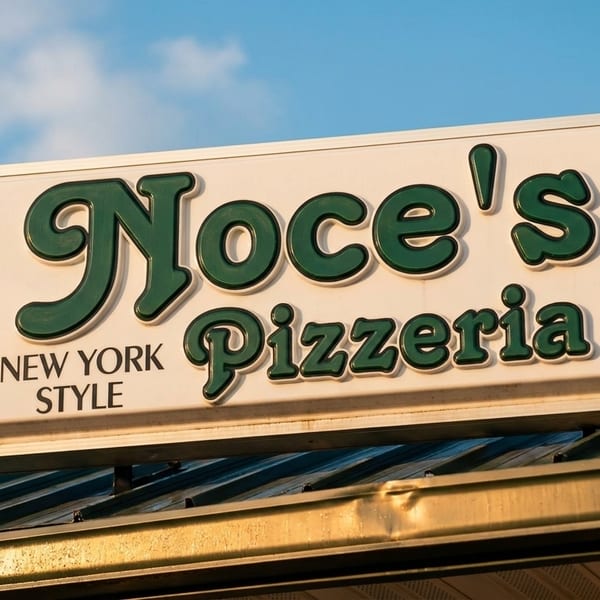 Noce's Pizzeria New York Style sign with green letters against a blue sky.
